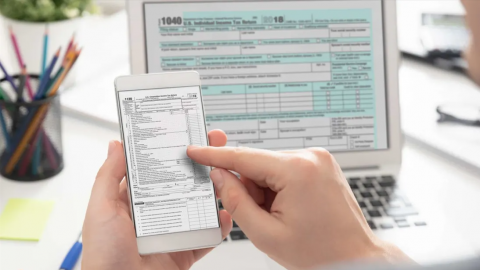 Person doing taxes on mobile phone and laptop computer